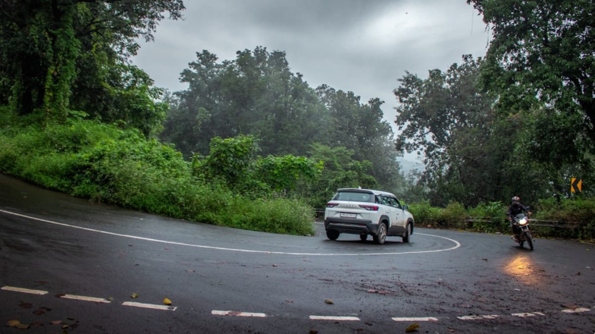 A woman driving during monsoon road trips in India, with misty green hills visible through the windshield