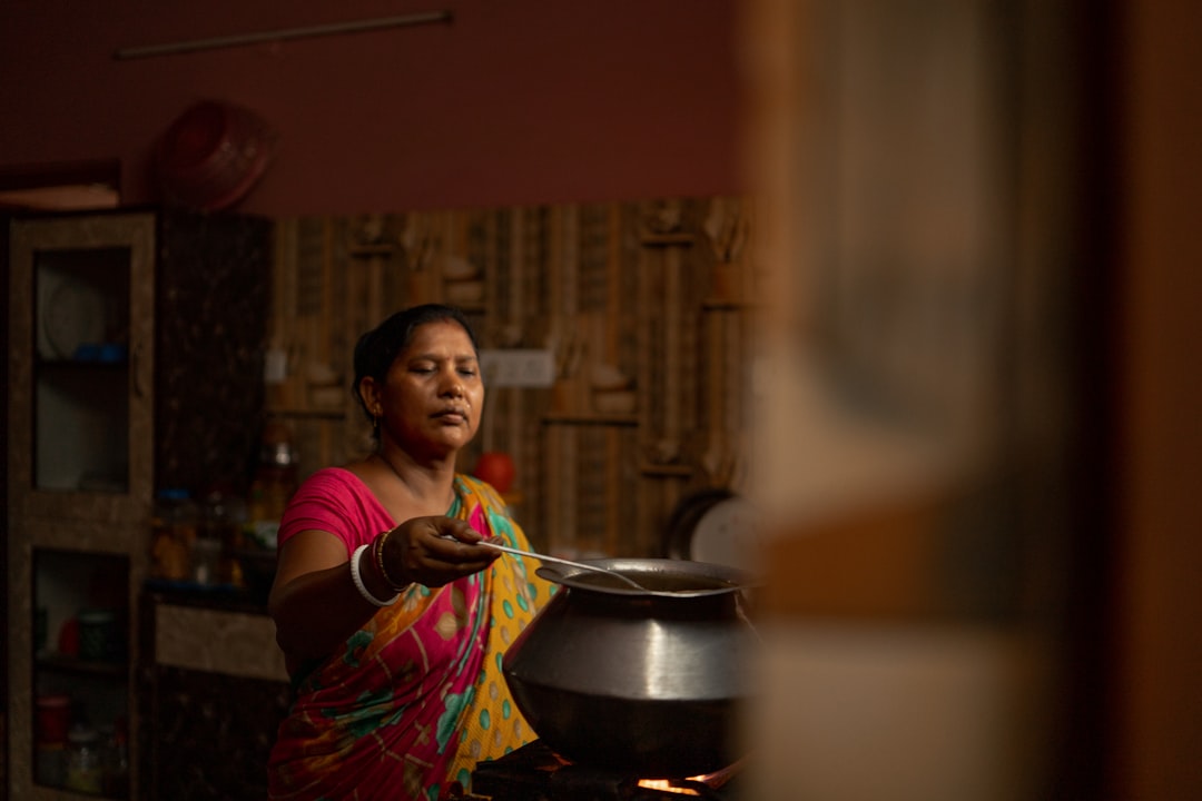 A smiling Indian woman enjoying a traditional plate of gluten-free food including dal and steamed rice at a kitchen table.