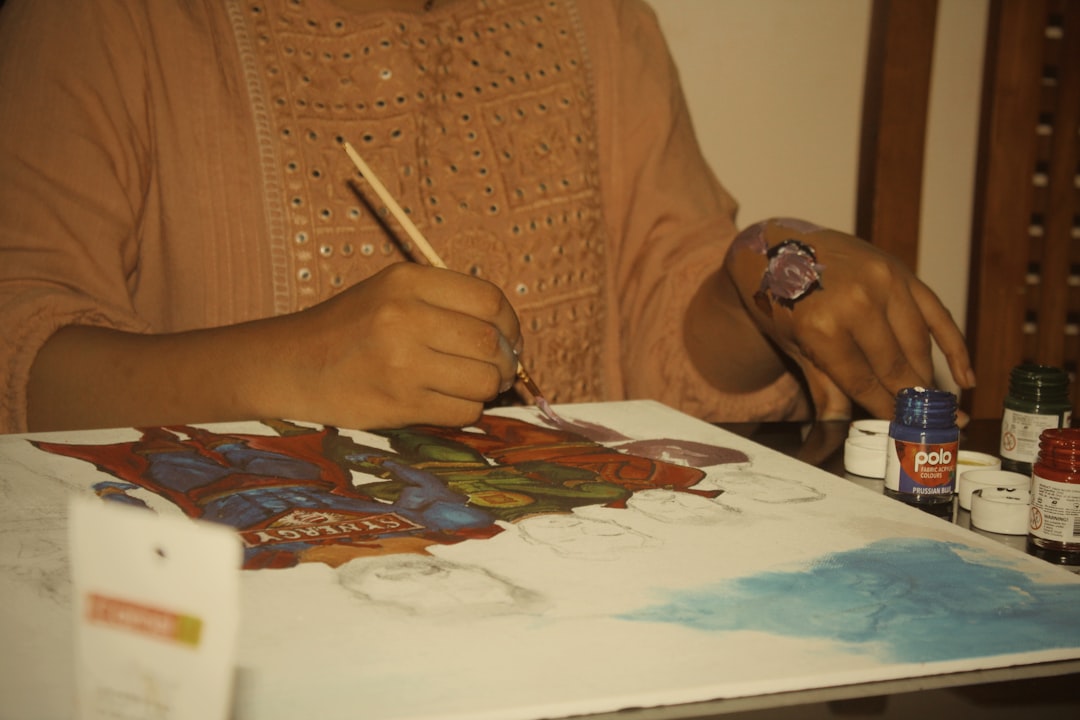 A woman carefully creating a Madhubani painting on thick white paper with a fine-tipped brush