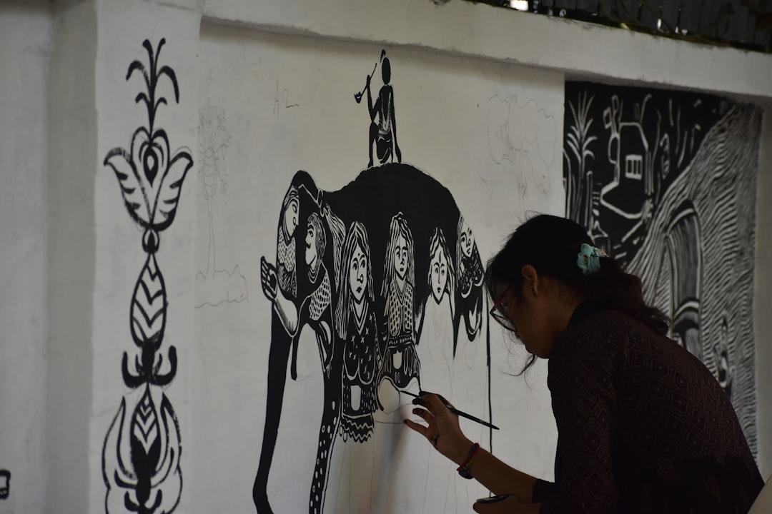 A woman in Maharashtra creating Warli art on brown paper using traditional white paint and a fine brush