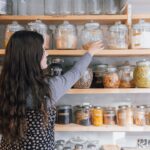 A woman carefully organising her home spice pantry with colourful Indian regional spices on a wooden shelf