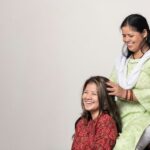 A woman performing a traditional scalp care oil massage on her long dark Indian hair at home