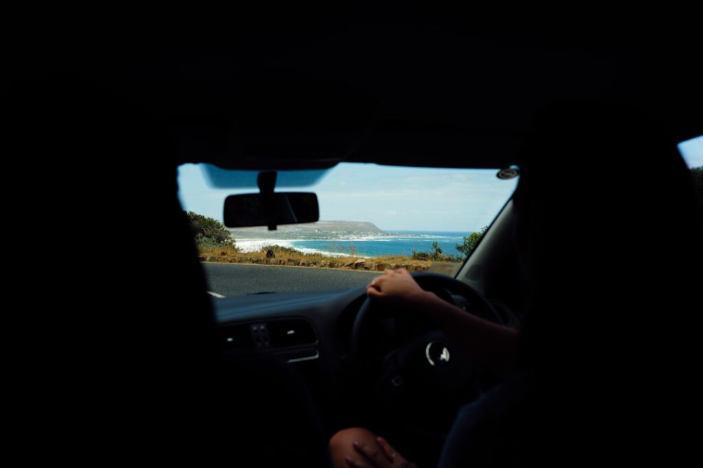 A traveller on the wheel enjoying coastal drives in India with green hills and the Arabian Sea visible through the windscreen