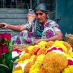 A woman carefully places flowers to create a pookalam design during the Onam festival celebration at her home entrance
