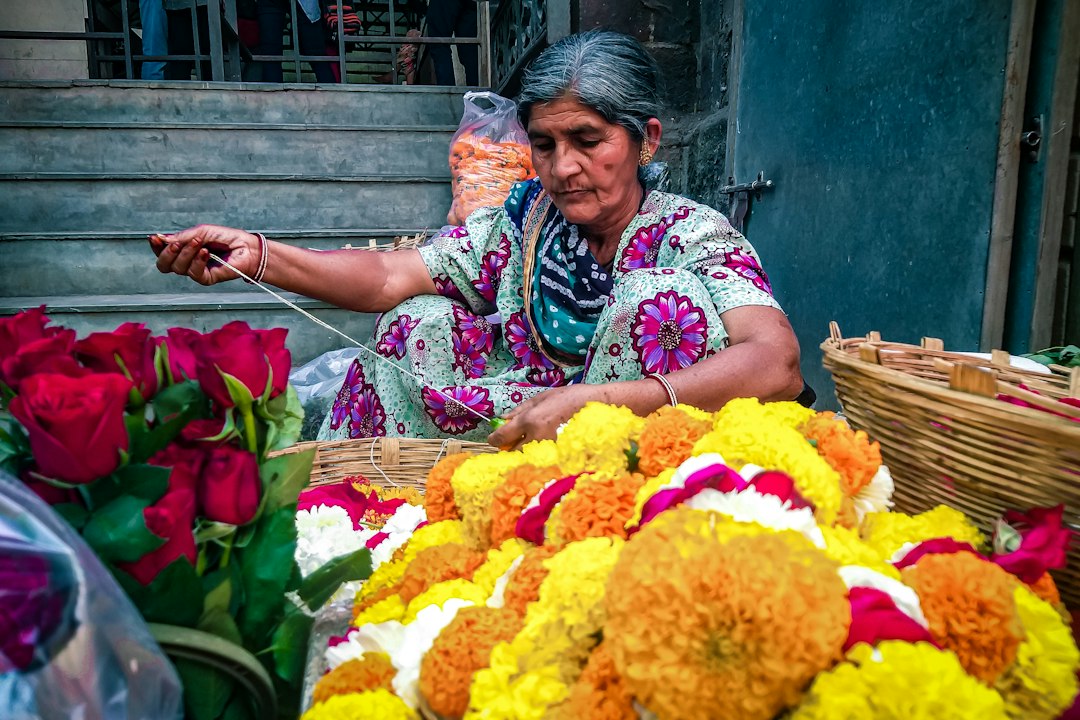 A woman carefully places flowers to create a pookalam design during the Onam festival celebration at her home entrance